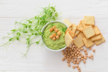 Bowl with tasty green pea hummus, chickpeas and crackers on light wooden background