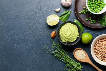 Composition with tasty green pea hummus, lime and chickpeas on dark background