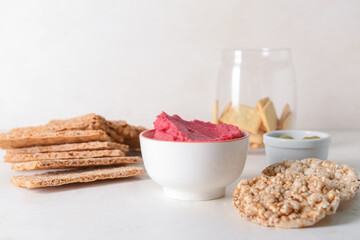 Bowl with tasty beet hummus and crackers on light background