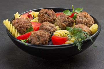Meatballs with tomatoes and pasta in black bowl.