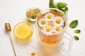 Composition with cup of chamomile tea, flowers, mint and honey on light background