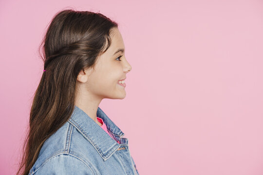 Side view of a profile of a beautiful teenage girl. Smiling girl on a pink background