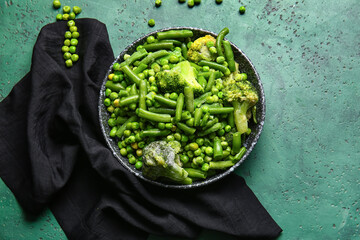 Plate with frozen green vegetables on color background