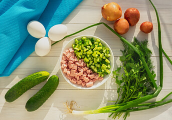 Okroshka. Summer dish of Russia. Ingredients for a traditional Russian cold soup. Sliced products. Top view. Cooking. Cucumbers, eggs, dill, onions, sour cream and kefir on a white wooden background.