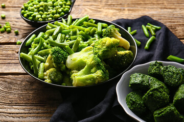 Bowls with frozen green vegetables on wooden background