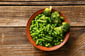 Bowl with frozen green vegetables on wooden background