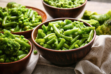 Bowls with frozen green vegetables on wooden background