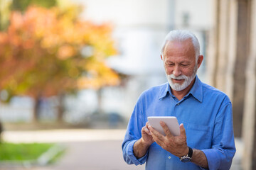 Handsome senior man with tablet in the street. Man using tablet in the public park. Senior businessman using a tablet in the city. Successful Modern Mature Businessman