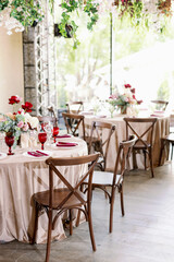 Rustic wooden chairs in wedding decor with red flowers and beige tablecloths.