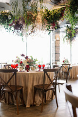 Elegant festive wedding decor with vintage wood chairs, powdery tablecloths and hanging flowers and foliage from the ceiling.