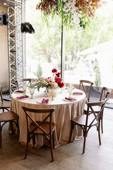 Decoration of the wedding table with red and pink flowers on a white tablecloth. Red glass goblets and burgundy napkins on the plates.