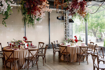 Elegant festive wedding decor with vintage wood chairs, powdery tablecloths and hanging flowers and foliage from the ceiling.