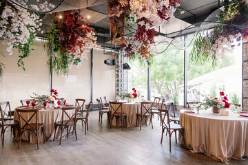 Elegant festive wedding decor with vintage wood chairs, powdery tablecloths and hanging flowers and foliage from the ceiling.