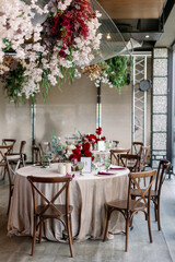 Dinner party indoors with served tables in a restaurant with red flowers and wooden vintage chairs in rustic boho style