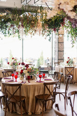Dinner party indoors with served tables in a restaurant with red flowers and wooden vintage chairs in rustic boho style