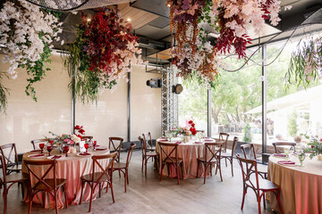Dinner party indoors with served tables in a restaurant with red flowers and wooden vintage chairs in rustic boho style