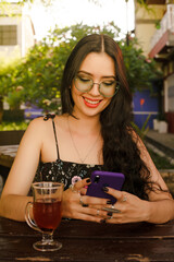 Young woman looks at her cell phone and sips tea in the open air