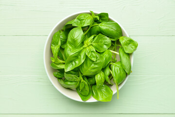 Bowl with fresh basil leaves on color wooden background