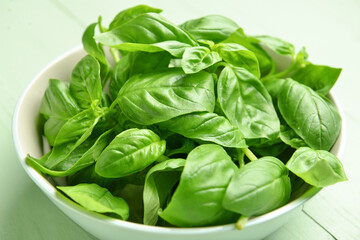 Bowl with fresh basil leaves on color wooden background, closeup