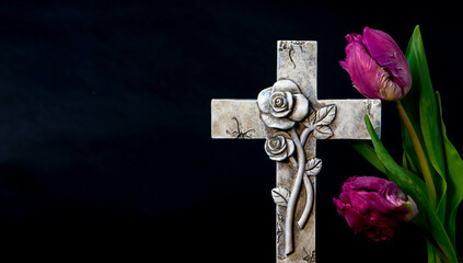 Isolated ornate religious cross with a tulip flower on a dark background. Moment of grief at the...