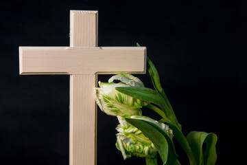 Isolated whithe religious wooden cross with tulip flowers on a dark background. Moment of grief at...