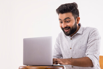 A BEARDED YOUNGSTER LOOKING AT LAPTOP IN EXCITEMENT