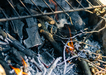 Charcoal and twigs burning under the metal grill grate 