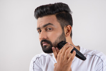 A YOUNG MAN USING TRIMMER ON HIS BEARD