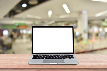 Laptop computer with blank screen on wood table over blur shopping mall background. Mock up, template for your design.