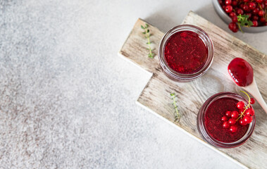 Homemade red currant jam or jelly in glass jars and red currants fresh berries on wooden cutting board. Top view. Copy space.