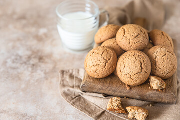Oatmeal cookies on wooden cutting board with a cup of milk, brown concrete background. Healthy snack or dessert.