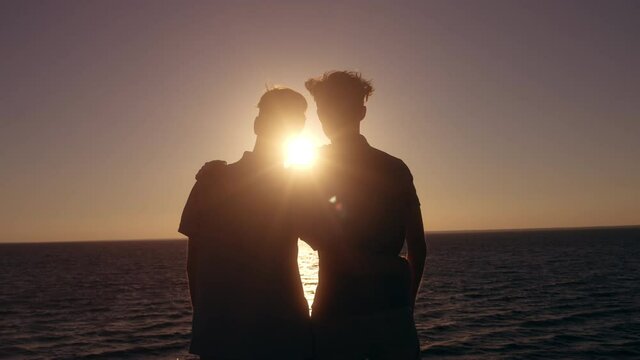 Silhouettes of gay couple enjoying romantic sunset over sea, hugging on date