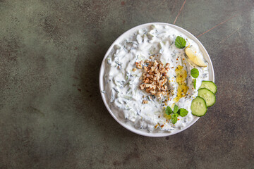 Traditional bulgarian cold summer soup tarator with ingredients on green background. Bulgarian soup with grated cucumbers, yogurt and walnuts. Top view.