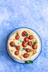 Savoury cheesecake with tomatoes decorated with mint, blue concrete background. Top view.