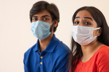 A young man and woman sitting together with masks on their face.