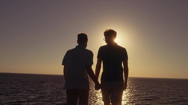 Two gay men holding hands smiling, enjoying beautiful sea view, romantic date