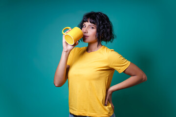 A young woman in yellow drinks from a cup of milk. Studio shot, isolated on a color background.