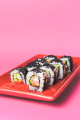 Tasty sushi roll maki with in red plate on pink background close up. Place for caption and text, copy space banner.