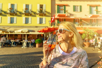 Woman tourist drinking a cocktail by the lakefront corniche in an open pub of Ascona historic city in Switzerland, in Ticino Canton on Lake Langensee.