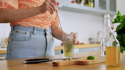 drinks and people concept - young woman with spoon making lime mojito cocktail at home kitchen