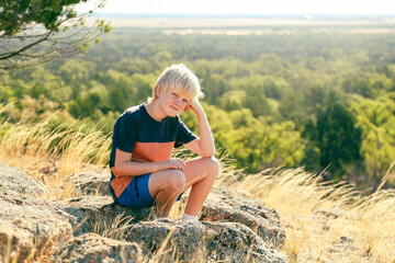 Naklejka na ściany i meble Young boy sitting on rock on hilltop with head resting on hand