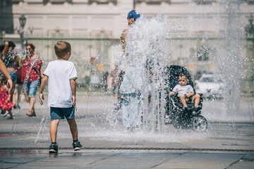 Fototapeta premium Kid or child playing with water near a fountain during hot summer day 