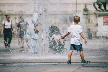 Kid or child playing with water near a fountain during hot summer day 