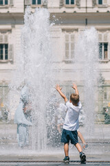 Kid or child playing with water near a fountain during hot summer day, vertical
