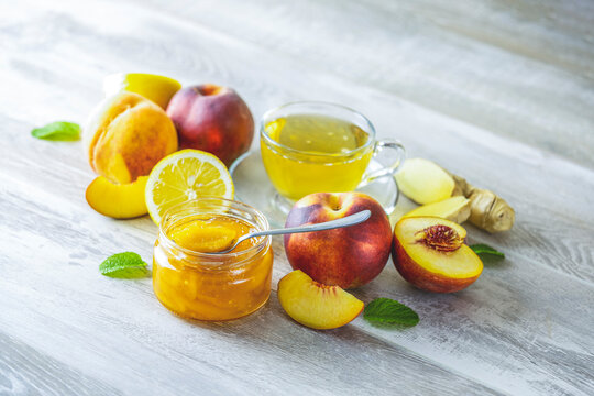 Fresh homemade peach jam in glass jar on a wooden background. Several fresh berries, lemon and mint are near it