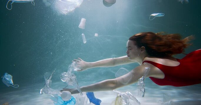 Cinematic under water side view, young beautiful female tourist swimming through plastic waste garbage slow motion.
