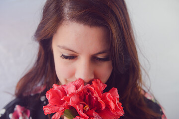 A close up portrait of a brunette woman smelling red flowers looking down