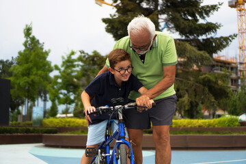 A boy is learning how to ride a bike with the help of his grandfather.
