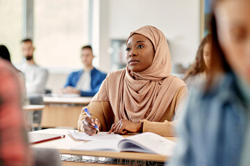 Young black student in hijab attending a class at university classroom.