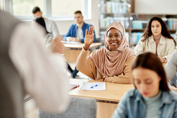 Happy African American student in hijab raising her had to ask a question during lecture at the...
